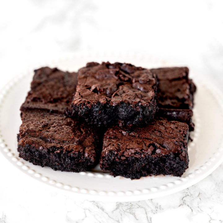 Dairy free brownies piled on a white plate sitting on a white marble counter