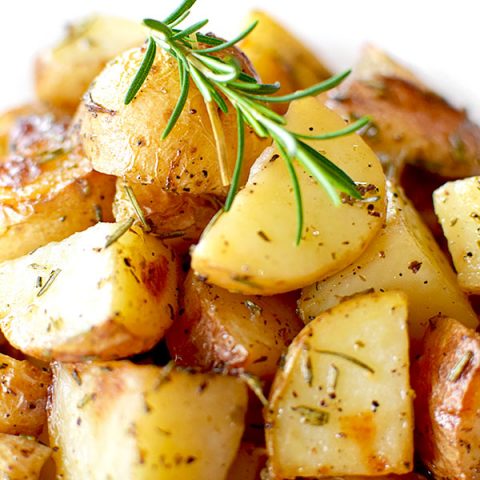 a pile of roasted potatoes with rosemary on a white plate