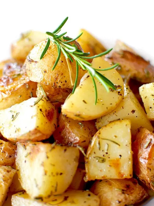 a pile of roasted potatoes with rosemary on a white plate