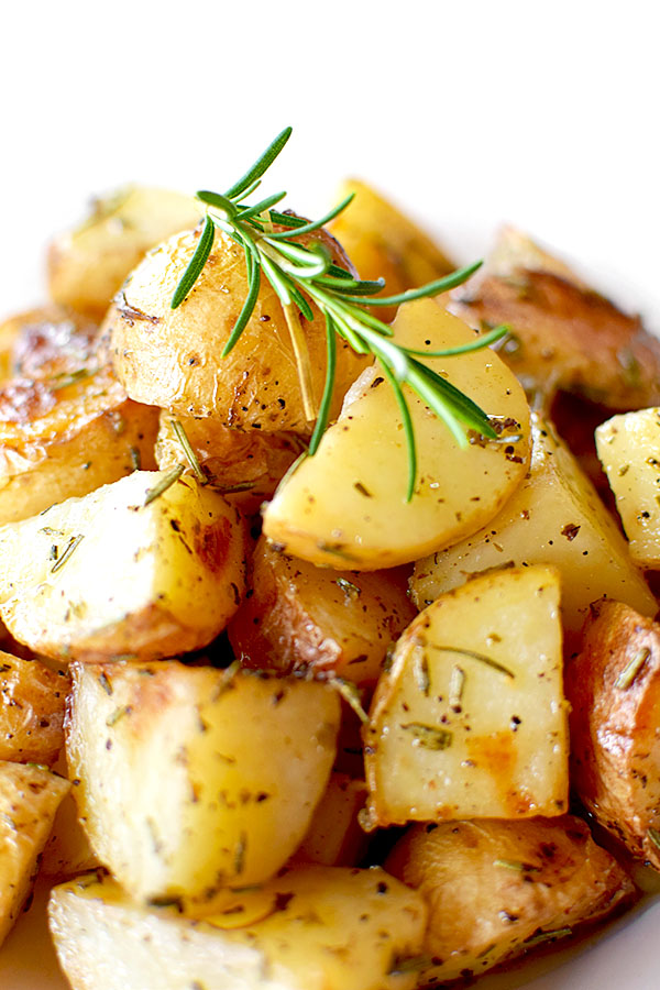 a pile of roasted potatoes with rosemary on a white plate