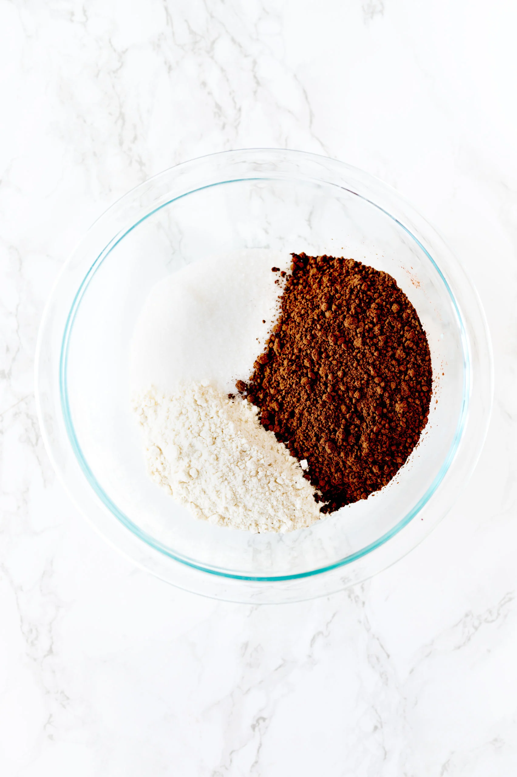 dry ingredients for dairy free brownie in a glass mixing bowl on a white marble counter