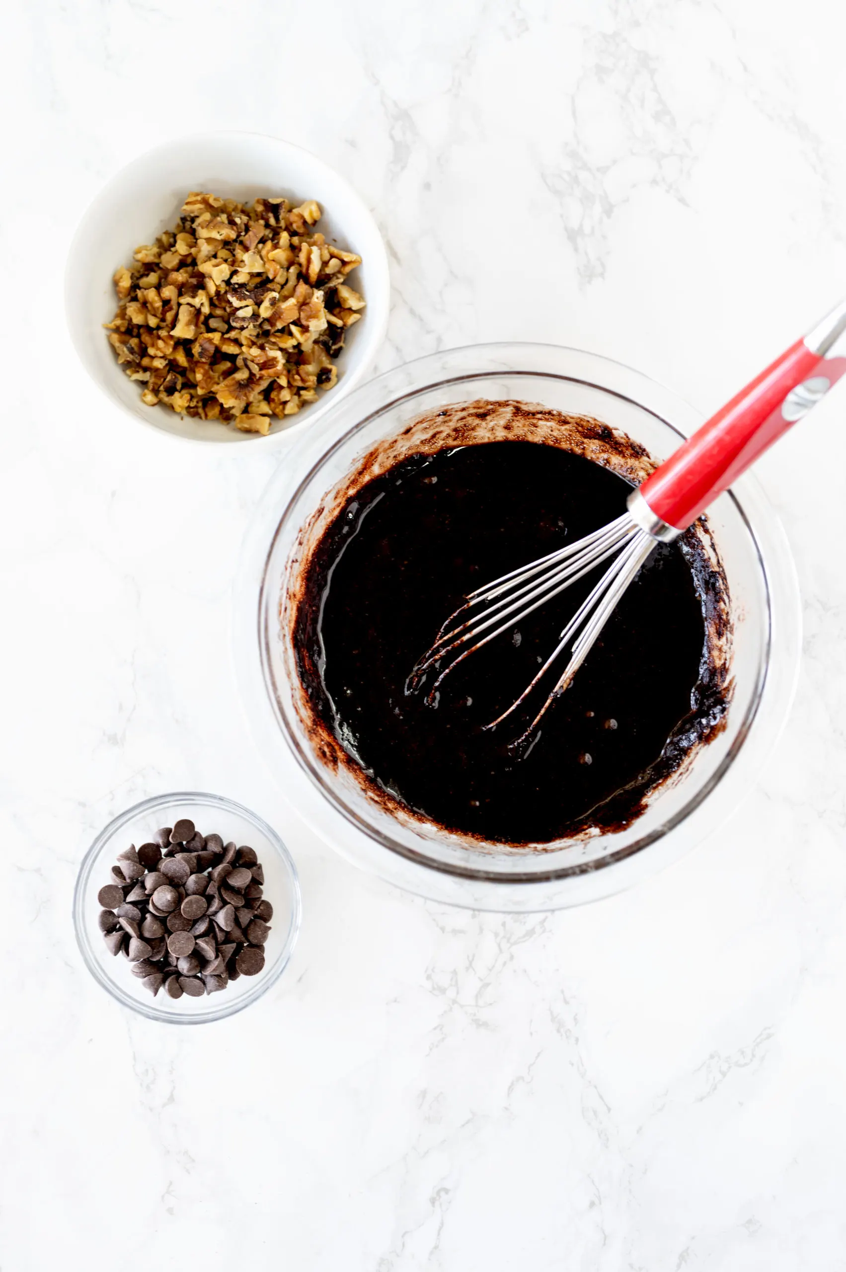 mixing bowl with dairy free brownie batter, and small bowls with nuts and chocolate chips on a counter