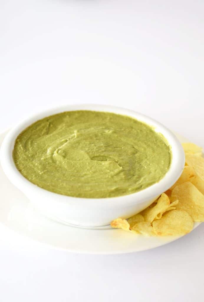 Avocado dip in a white bowl with potato chips on the side