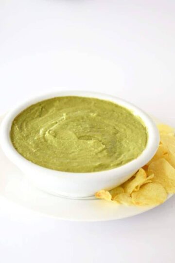 Avocado dip in a white bowl with potato chips on the side