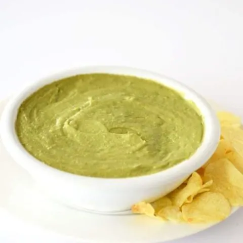 Avocado dip in a white bowl with potato chips on the side