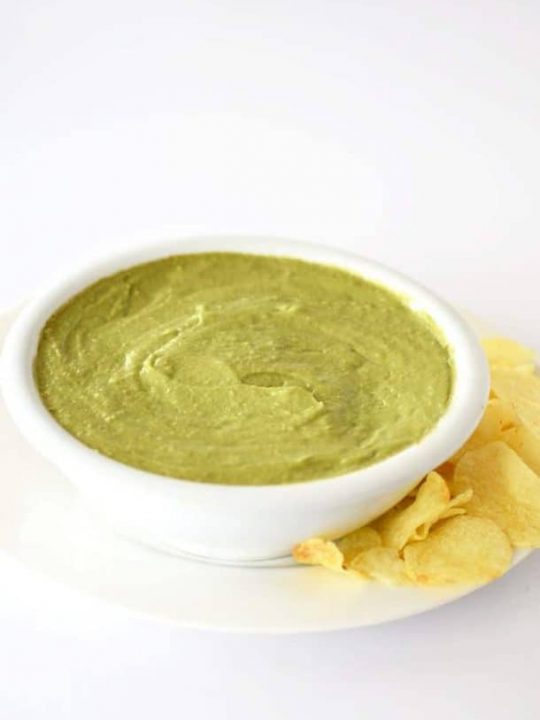 Avocado dip in a white bowl with potato chips on the side