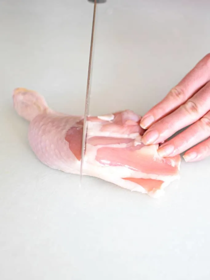 Knife cutting chicken leg where the drumstick meets the thigh