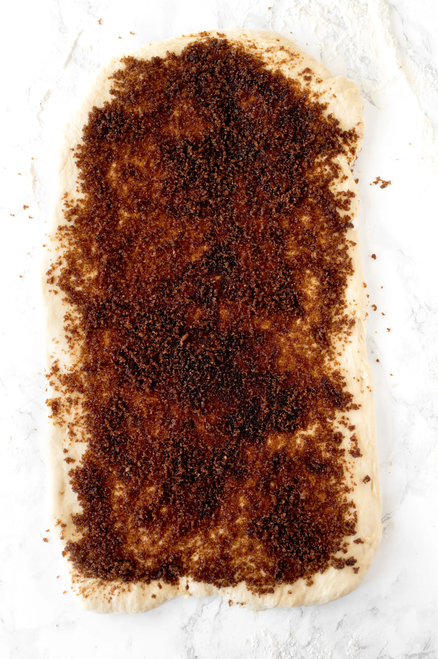 cinnamon roll dough rolled out into a rectangle with brown sugar mixture spread on it