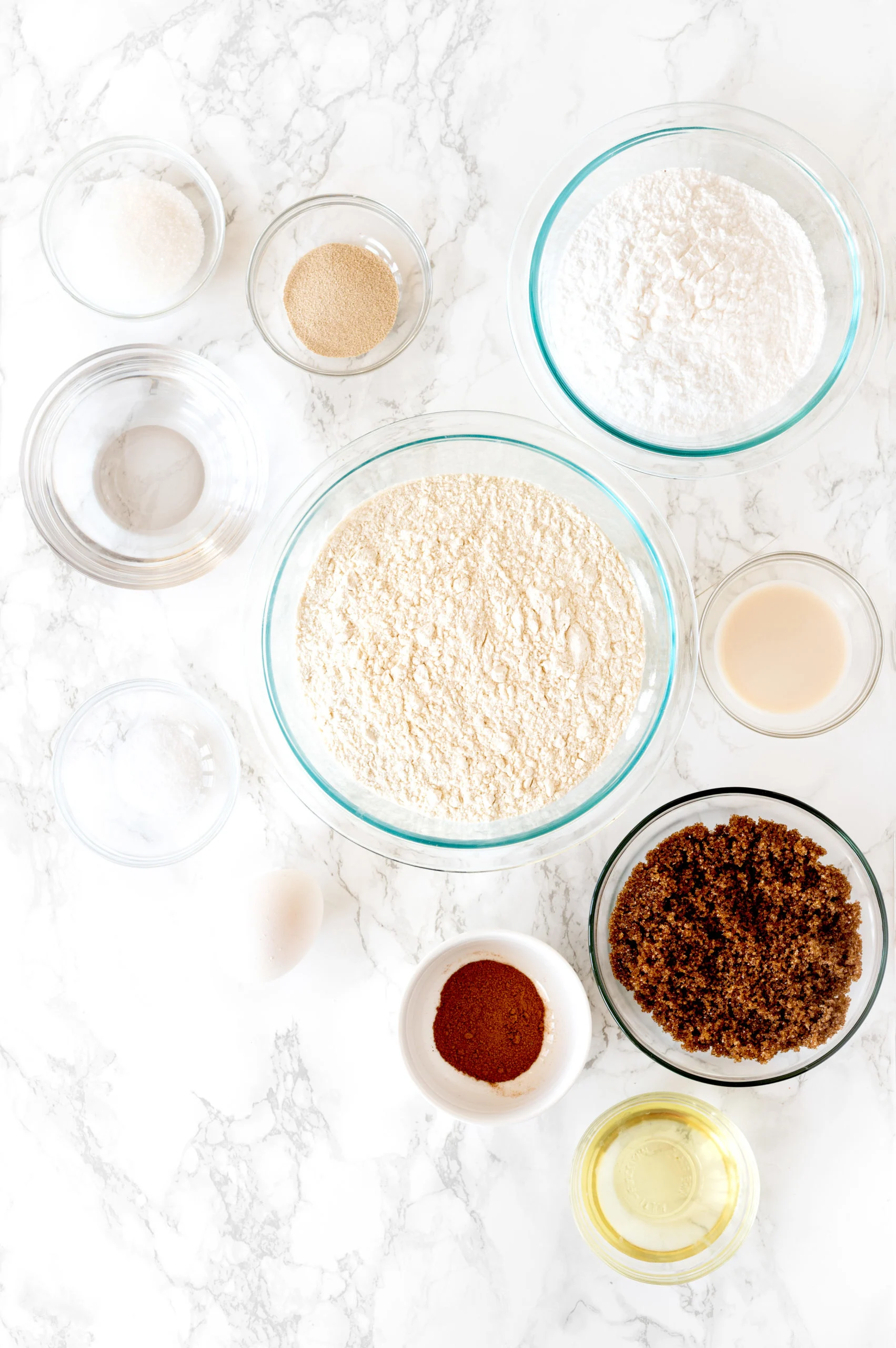 ingredients for cinnamon rolls in glass bowls on white marble counter