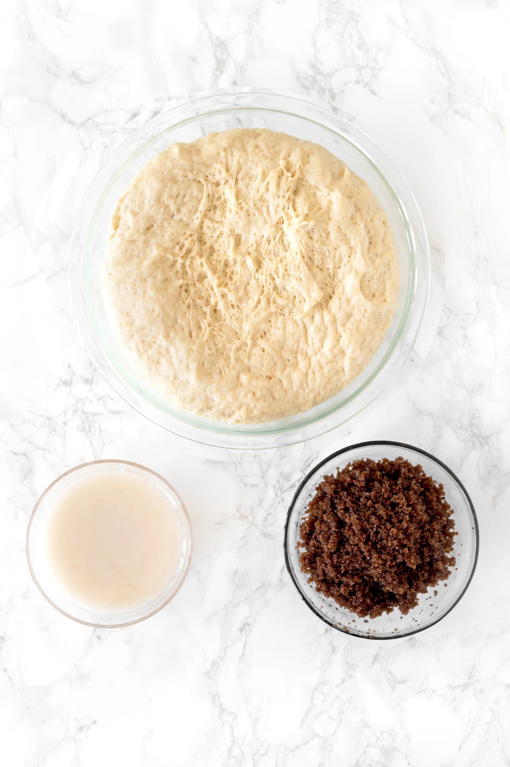 mixed ingredients for cinnamon rolls in glass bowls on white marble counter