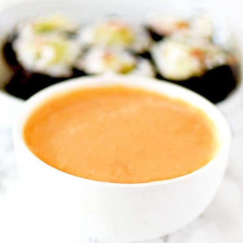 Spicy mayo in a dipping bowl with sushi in the background