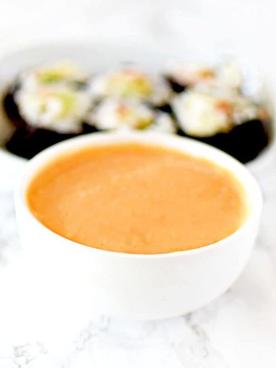 Spicy mayo in a dipping bowl with sushi in the background