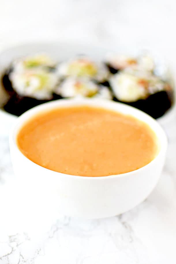Spicy mayo in a dipping bowl with sushi in the background
