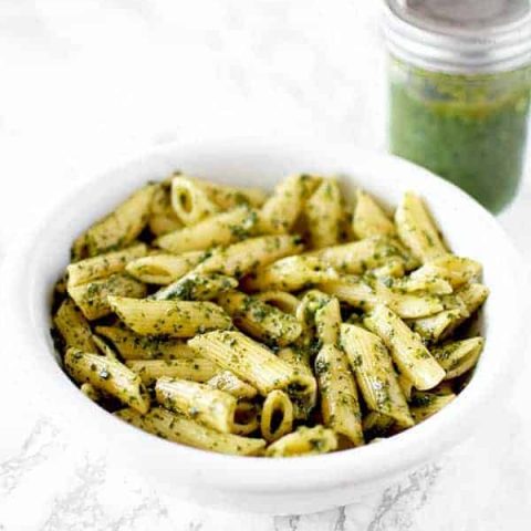 a bowl of dairy free (vegan) pasta with pesto and a jar of pesto sauce in the background