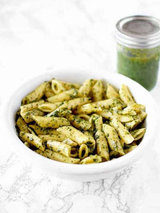 a bowl of dairy free (vegan) pasta with pesto and a jar of pesto sauce in the background