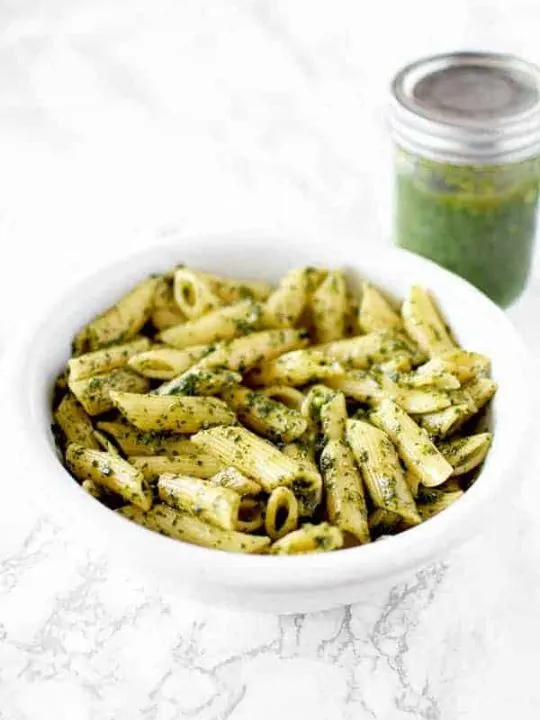 a bowl of dairy free (vegan) pasta with pesto and a jar of pesto sauce in the background