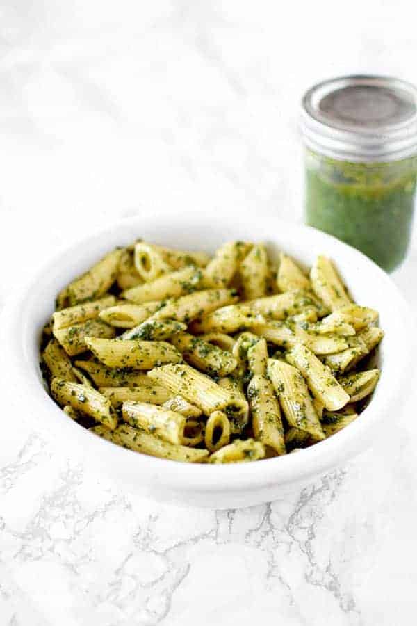 a bowl of dairy free (vegan) pasta with pesto and a jar of pesto sauce in the background