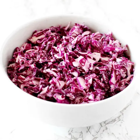 Israeli red cabbage salad in a white bowl on a white marble counter