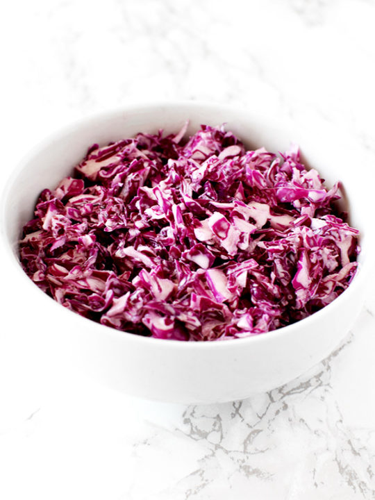 Israeli red cabbage salad in a white bowl on a white marble counter