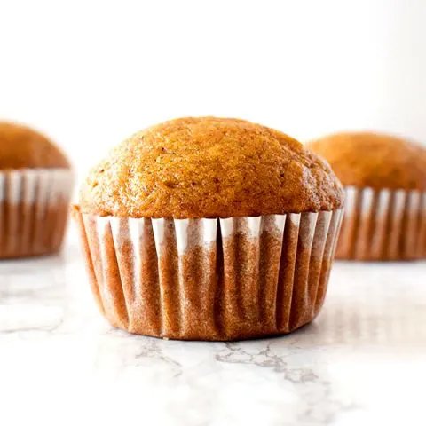 Three butternut squash muffins sitting on a white marble counter