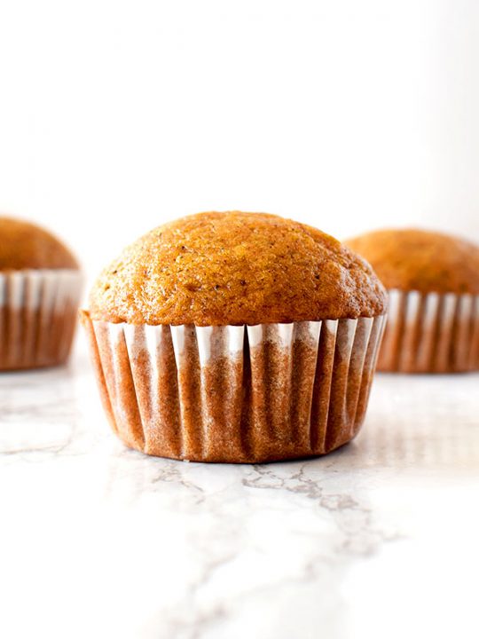 Three butternut squash muffins sitting on a white marble counter