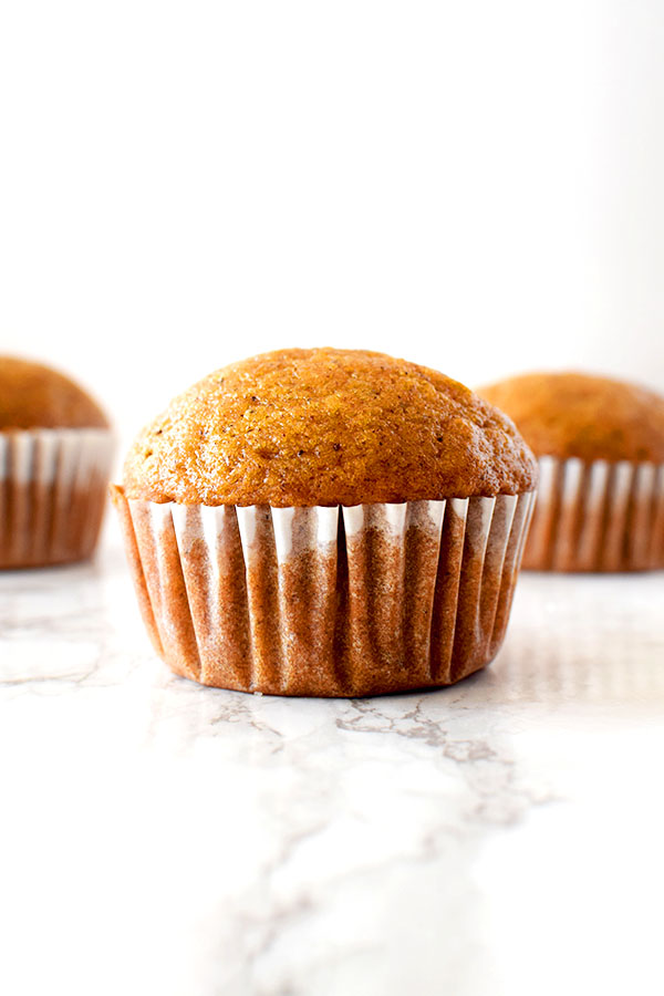 Three pumpkin muffins sitting on a white marble counter