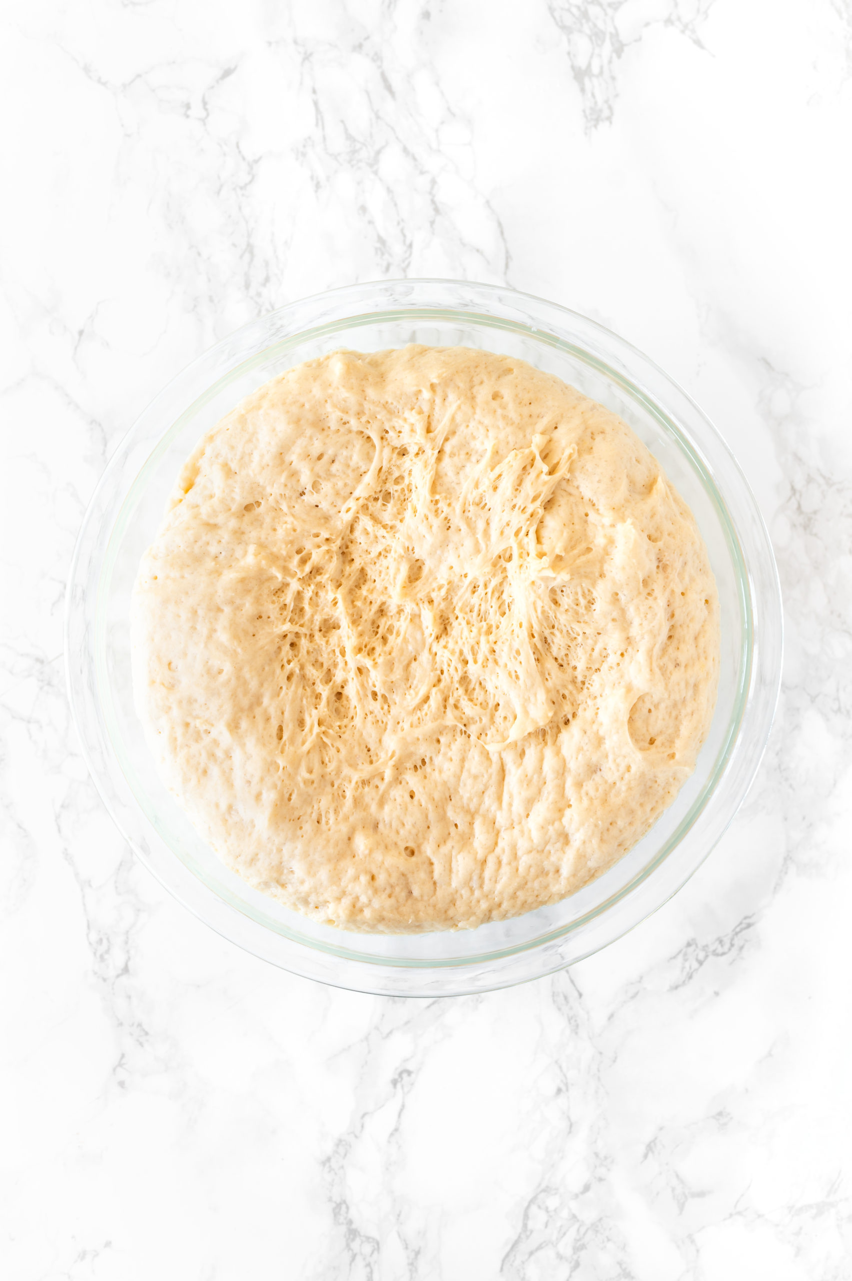 challah dough in a glass bowl on a white marble counter