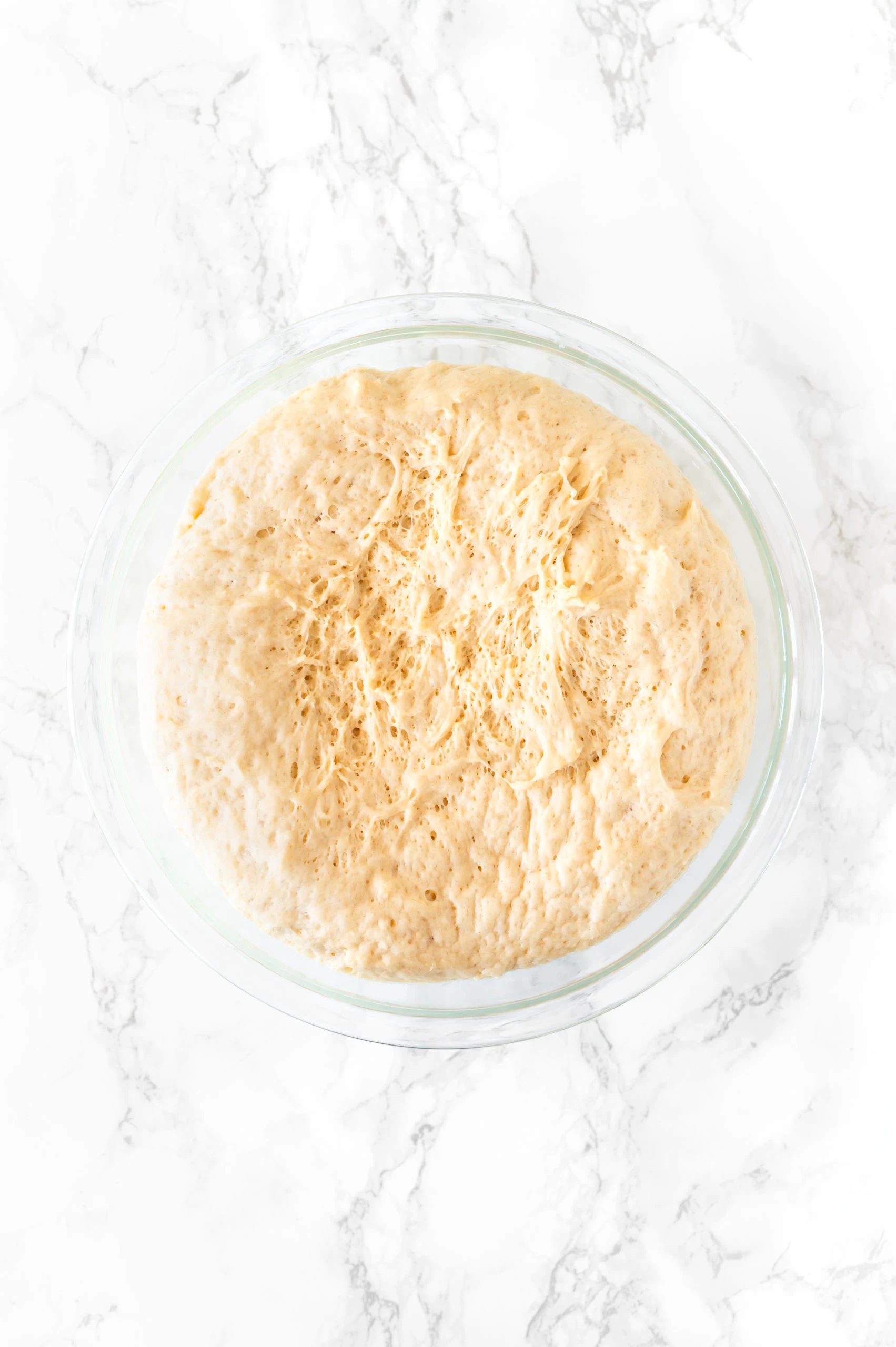 challah dough in a glass bowl on a white marble counter