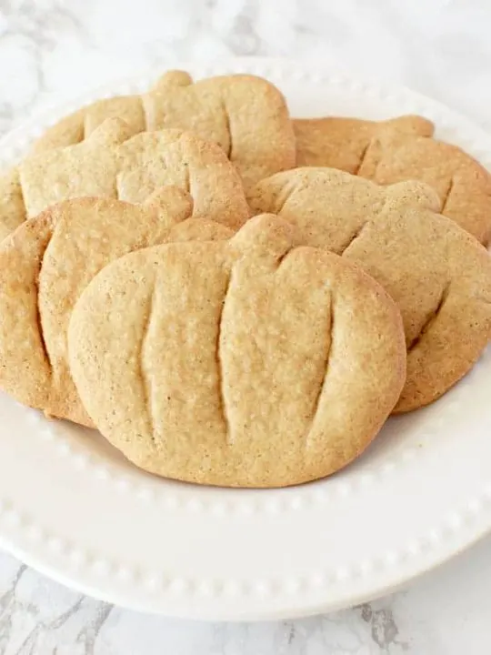 pumpkin spice cookies cut into pumpkin shapes on a white plate
