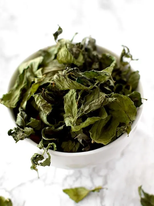 dried mint leaves in a white bowl on a counter