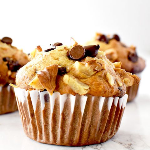 three chocolate chip banana nut muffins on a white marble counter