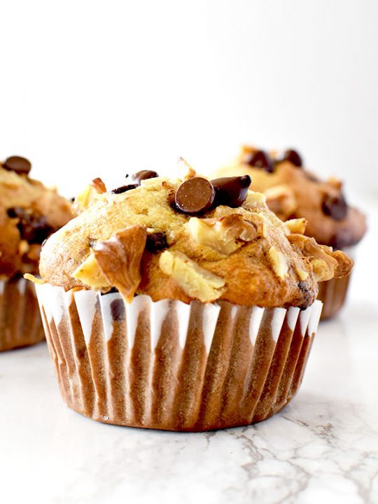 three chocolate chip banana nut muffins on a white marble counter