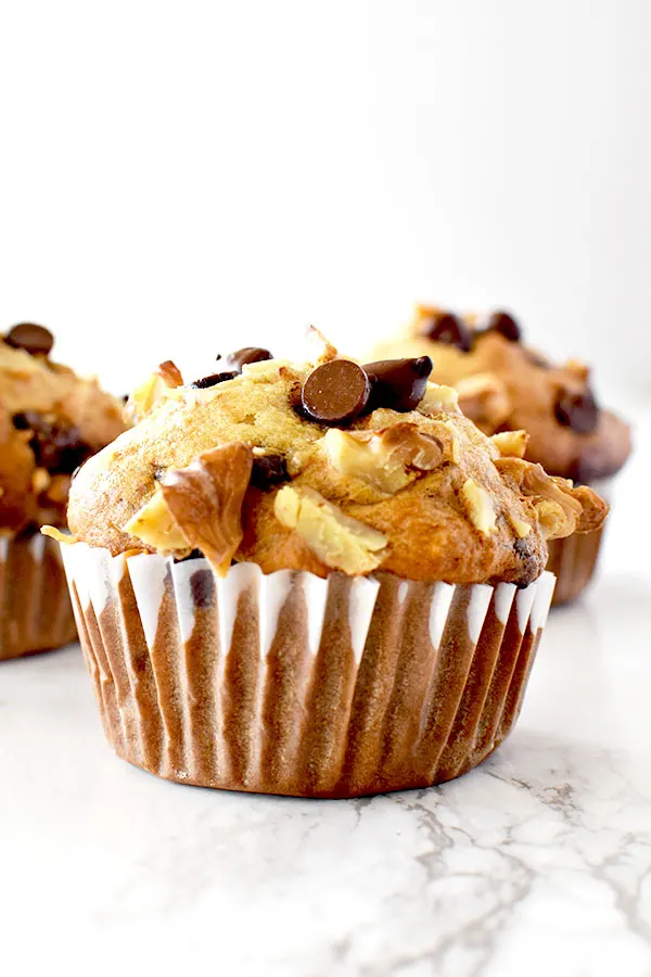 three chocolate chip banana nut muffins on a white marble counter