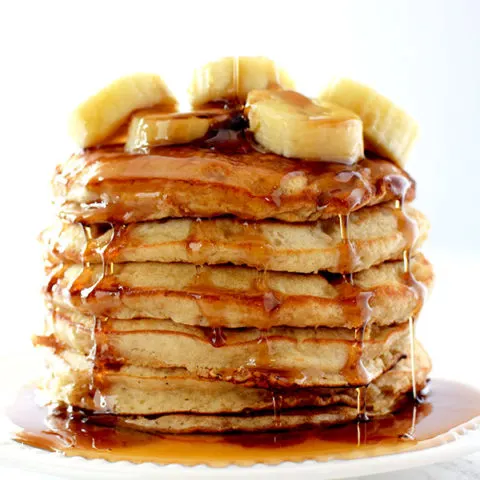 Stack of banana pancakes topped with bananas and dripping in maple syrup