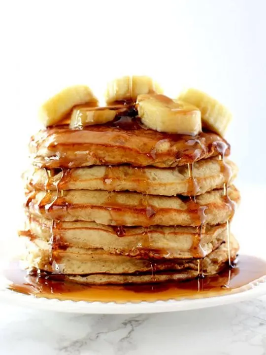 Stack of banana pancakes topped with bananas and dripping in maple syrup