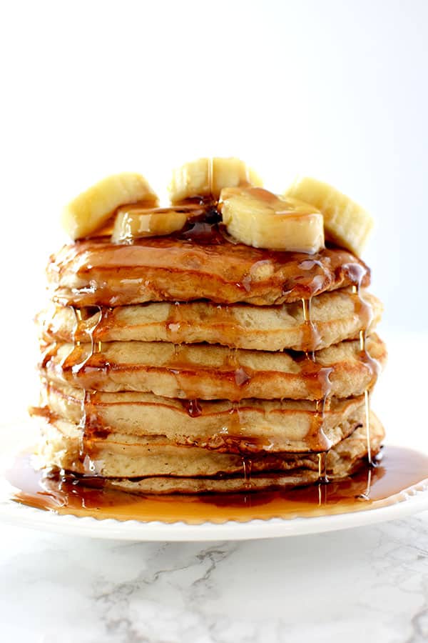 Stack of banana pancakes topped with bananas and dripping in maple syrup