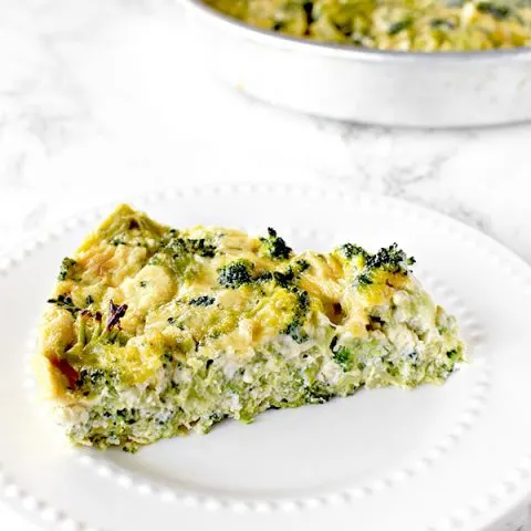 slice of broccoli kugel on a white plate with a pan of broccoli kugel in the background