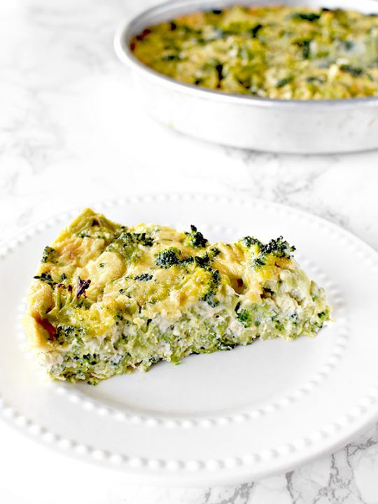 slice of broccoli kugel on a white plate with a pan of broccoli kugel in the background