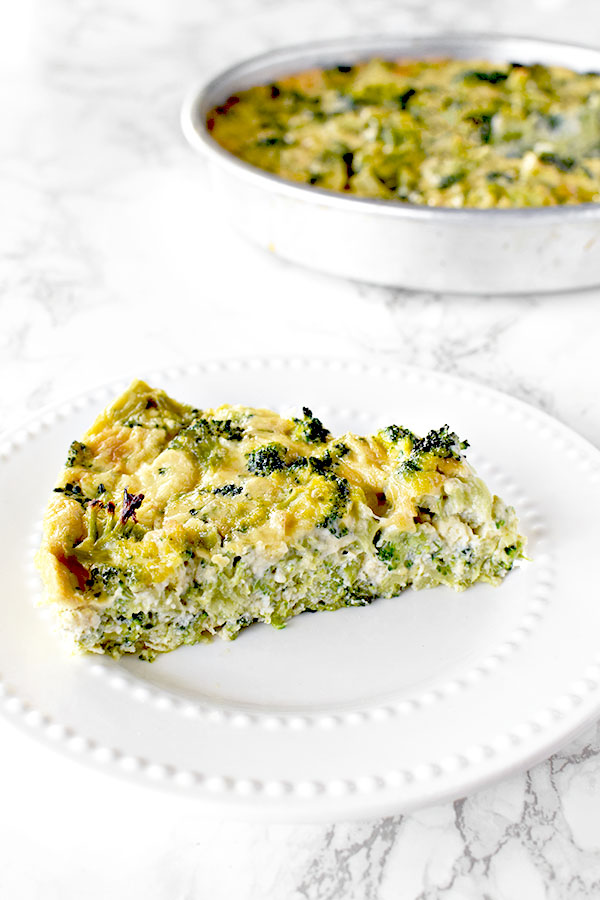 slice of broccoli kugel on a white plate with a pan of broccoli kugel in the background