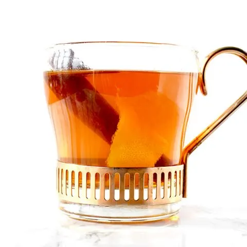 glass cup filled with mulled apple juice, a cinnamon stick, and an orange peel