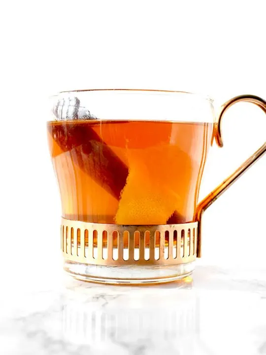 glass cup filled with mulled apple juice, a cinnamon stick, and an orange peel