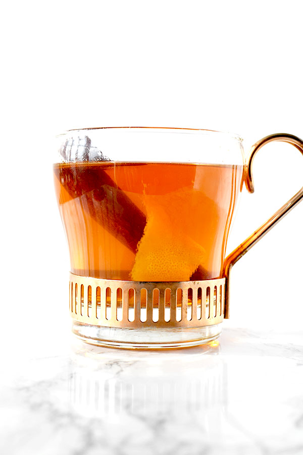 glass cup filled with mulled apple juice, a cinnamon stick, and an orange peel