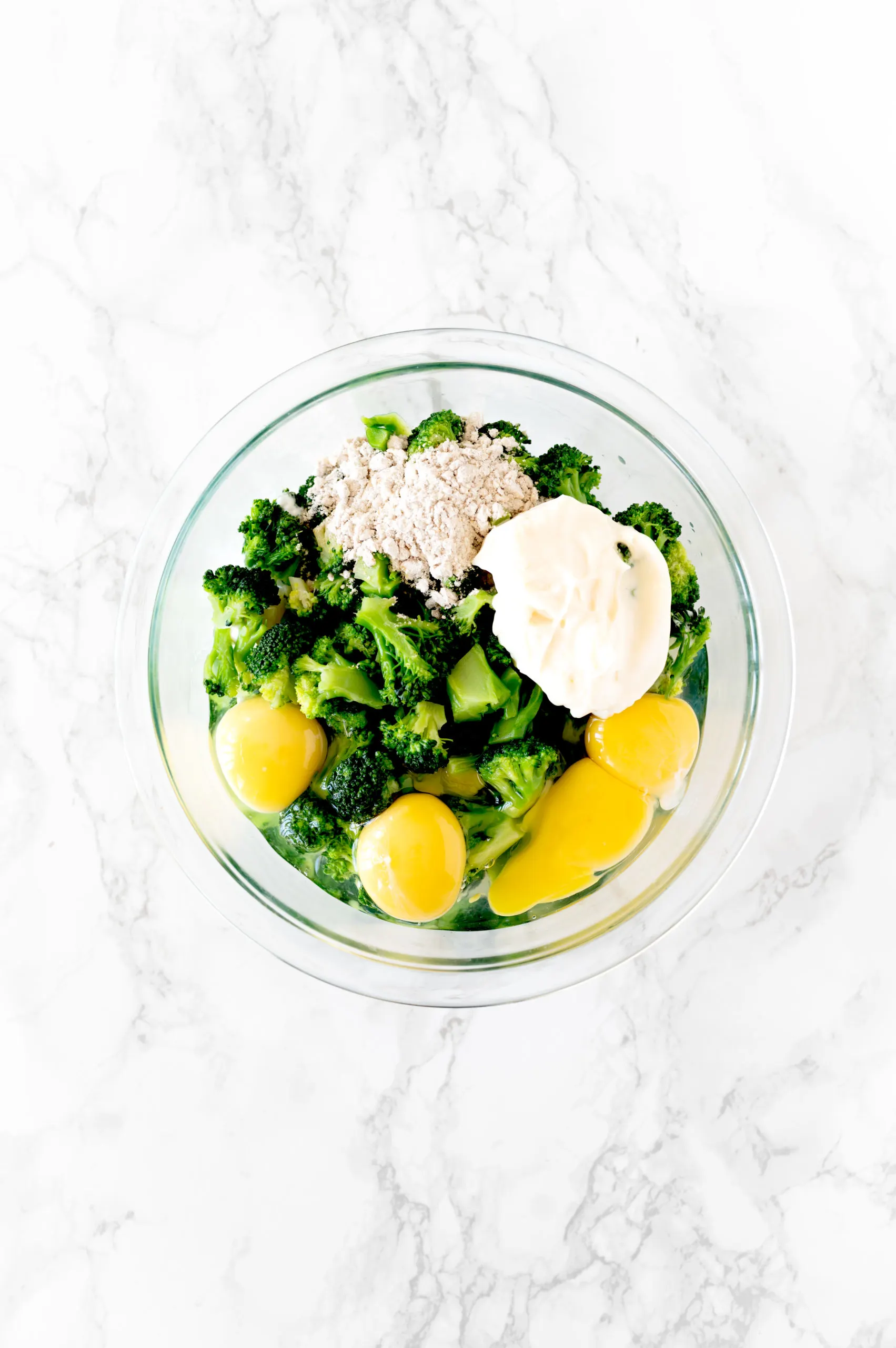 ingredients for broccoli kugel in a bowl on a white marble counter