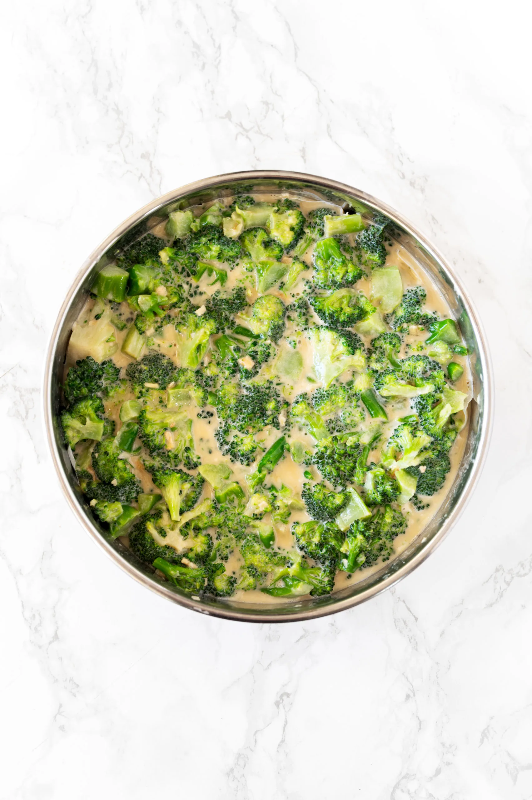 broccoli kugel mixture in a round pan on a white marble counter
