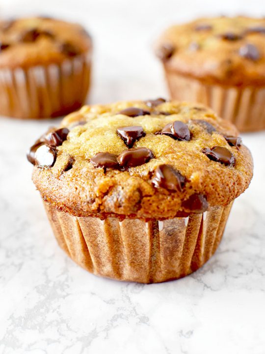 moist three banana chocolate chip muffins on a white marble counter