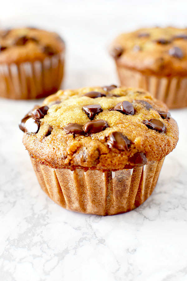 moist three banana chocolate chip muffins on a white marble counter