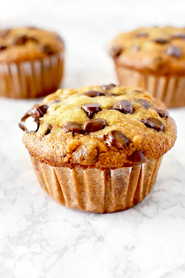 moist three banana chocolate chip muffins on a white marble counter