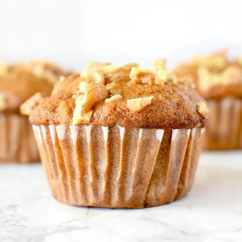 Three banana nut muffins on a white marble counter