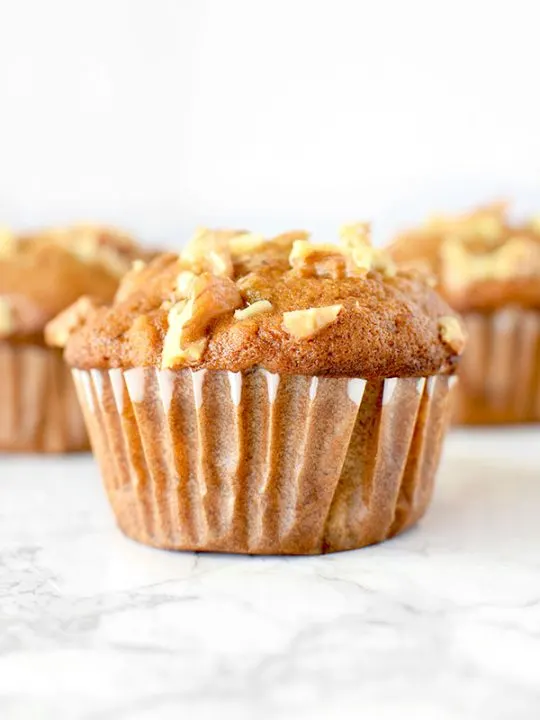 Three banana nut muffins on a white marble counter