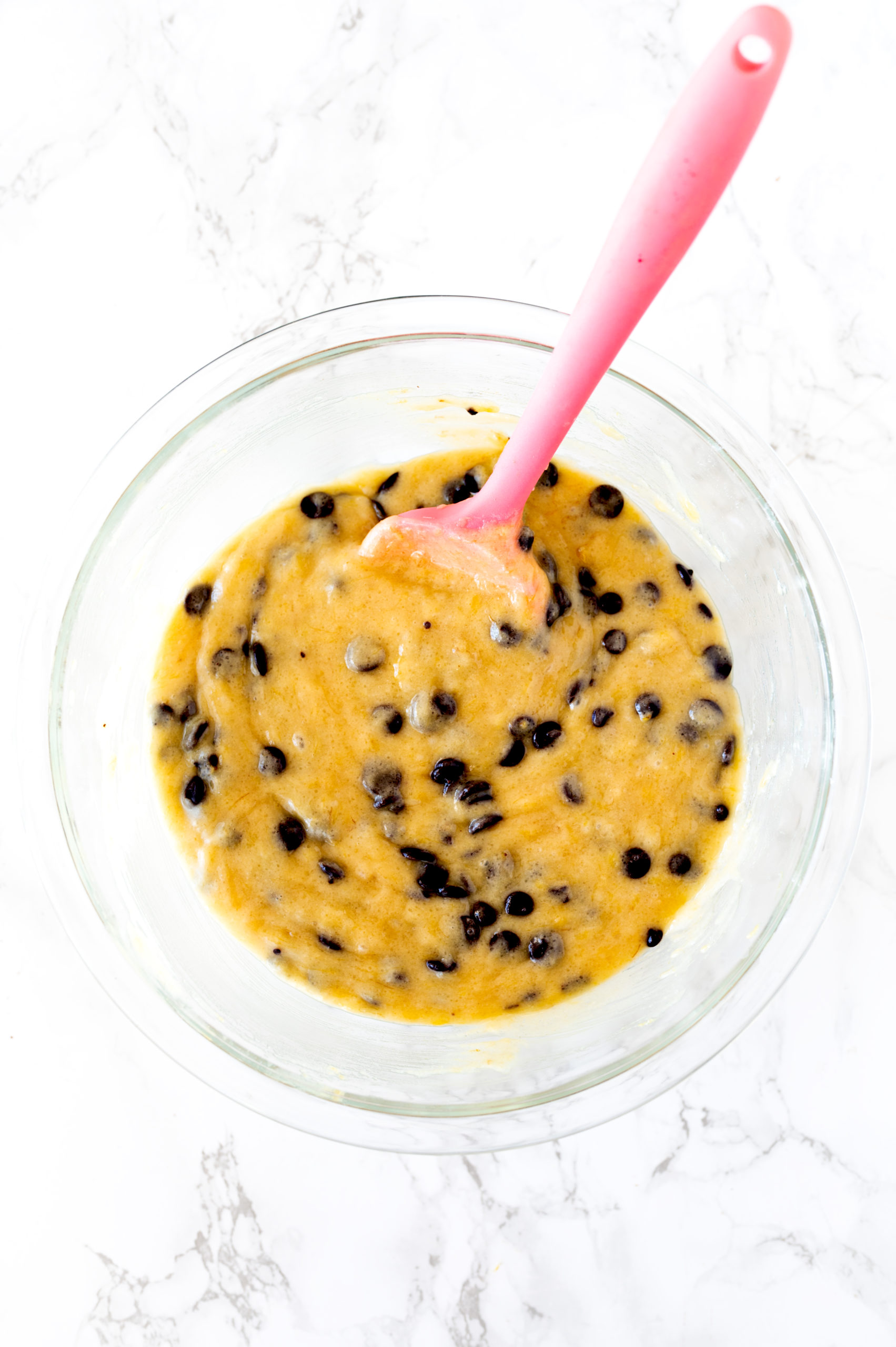 banana chocolate chip batter in a mixing bowl on a white marble counter